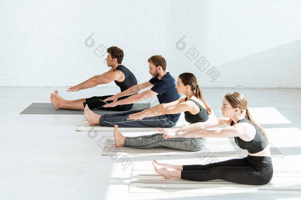 穿着运动服坐在前排弯腰练习瑜伽的年轻人