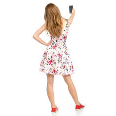 美丽的女人在礼服与鲜花打印和运动鞋显示积极的情绪与智能手机手机自拍