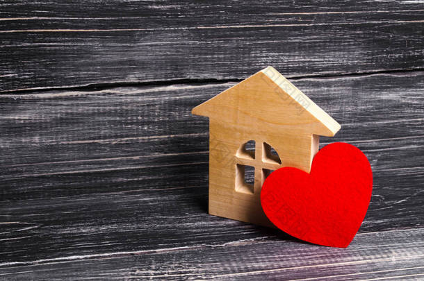 木房子与一个红色的心在黑暗的木质背景。给恋人的房子, 蜜月。为年轻家庭购买自己负担得起的住房。规划家庭和后代