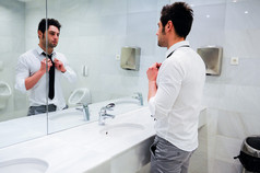 在公共厕所用镜子穿衣服的男人