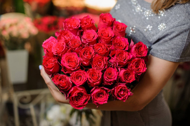 穿着灰色礼服的女人捧着一束美丽的粉红色玫瑰花