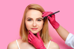 美容专家矫正眉毛形状与棕色化妆铅笔反对粉红色背景