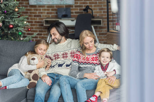 快乐的家庭与二个孩子坐在一起在沙发在圣诞节时间 