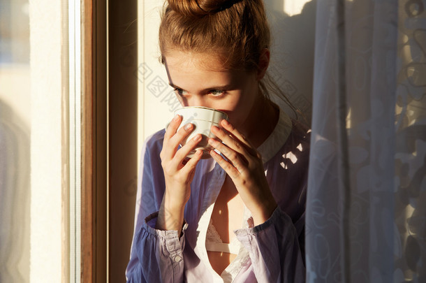 美丽的女人坐在窗边的早晨喝咖啡.