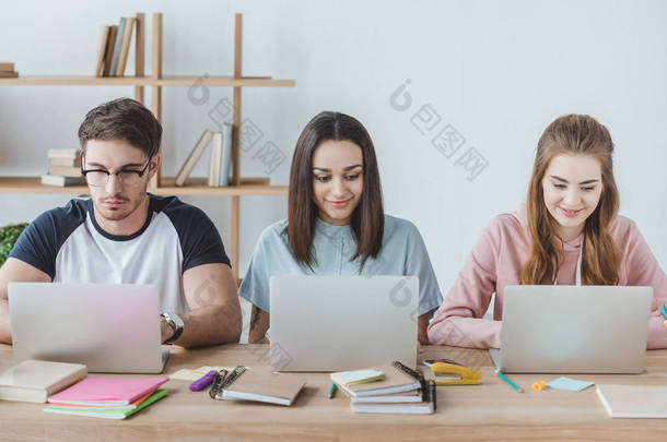 多民族学生坐在桌边看书时使用笔记本电脑