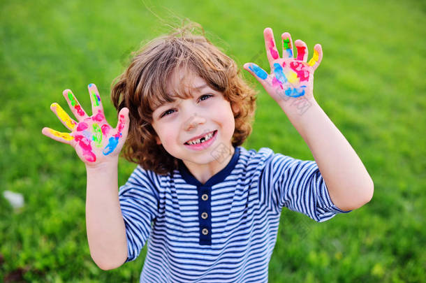 没有前牙的卷发的男孩显示手肮脏用多色的手指油漆和微笑.