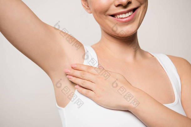 面带微笑的女人在灰色隔离的腋下涂除臭剂