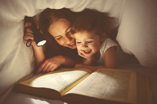 家庭阅读的就寝时间。妈妈和孩子读书与 flashl