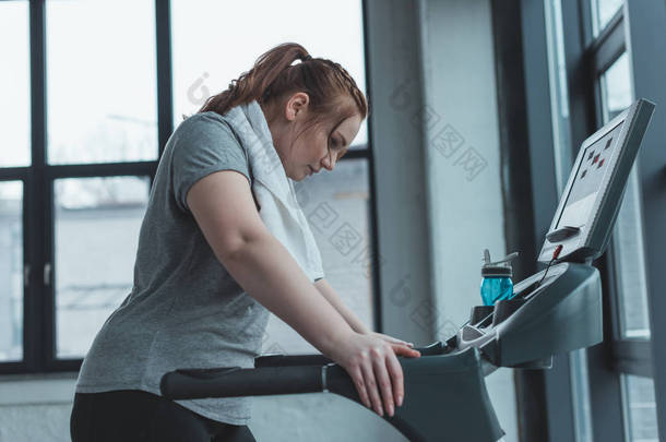 肥胖女孩休息在跑步机在健身房