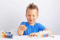 快乐快乐的小男孩，头发凌乱，手里拿着一把刷子，画着金色的颜料。学校教育或幼儿园教育概念.