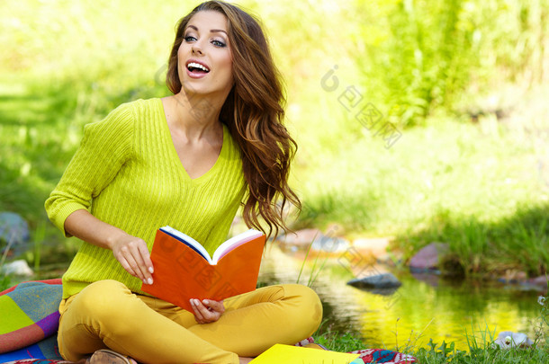 年轻漂亮的女人在绿色的原野上奠定了和看书.