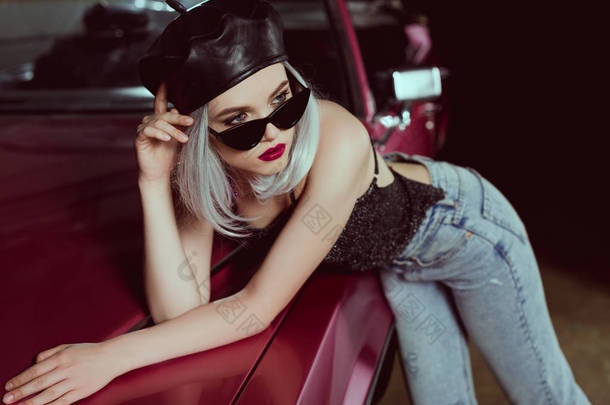 美丽的时尚金发女郎在太阳镜和黑色贝雷帽倚在车上, 看<strong>着</strong>远离