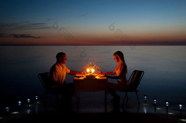 一对年轻夫妇在海滩上蜡烛与共享浪漫的晚餐