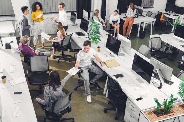 在开放空间办公室使用纸张和计算机的专业年轻同事的高角度视角 