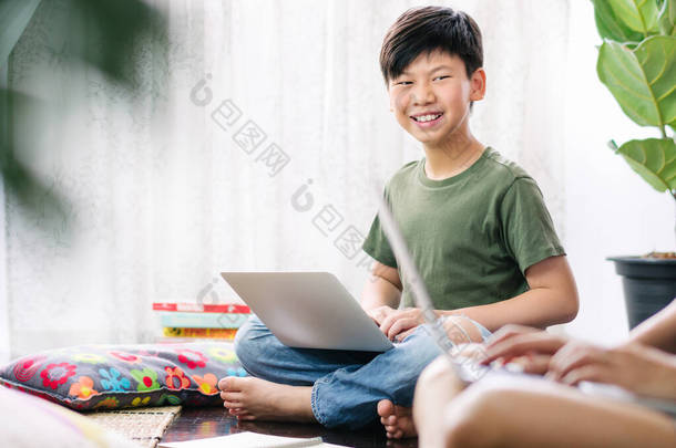 聪明的亚洲少年使用电脑笔记本电脑，坐在木制地板上，笑着，与朋友讨论小组<strong>工作</strong>、家庭作业、考试准备等问题。小组<strong>工作</strong>与协作.
