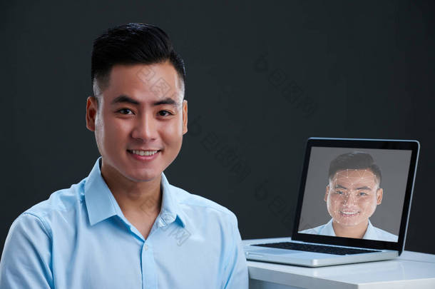 微笑的亚洲男子看着相机, 笔记本电脑与亚洲商人的照片