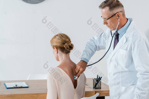 医生在眼镜使用听诊器,而检查妇女在诊所 