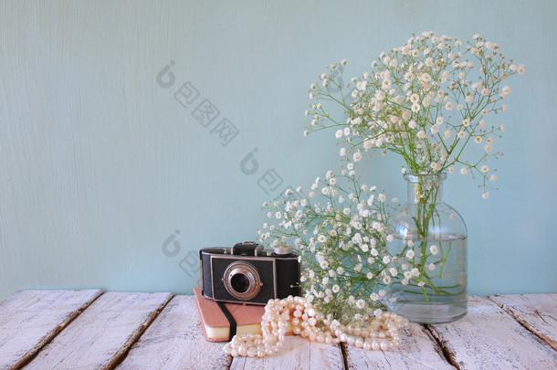 old notebook, white pearls necklace next to old photo camera on wooden table