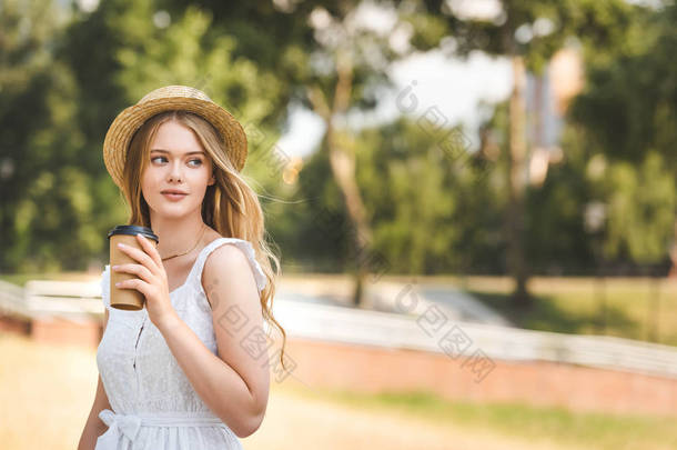 美丽的女孩<strong>在</strong>白色礼服和草帽拿着纸咖啡杯，看着远