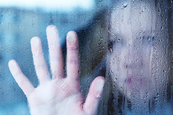 忧郁和悲伤的年轻女子在雨中的窗口