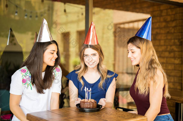 戴着派对帽的漂亮年轻女子在餐厅和朋友一起庆祝生日