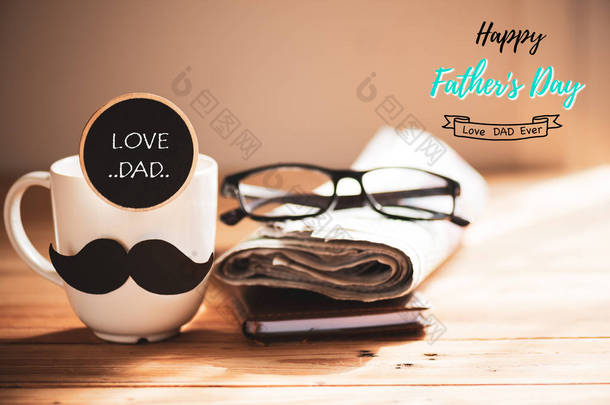 快乐的父亲日概念。咖啡杯与黑纸胡子, 木标记与愉快的父亲天文本和报纸, 笔记书, 杯子在木桌背景.