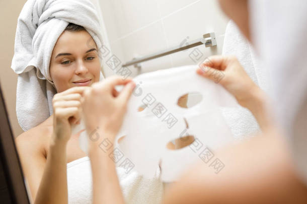 妇女在浴室是应用面部床单面具