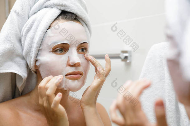 妇女在浴室是应用面部床单面具