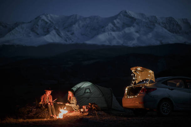 夫妇在露营与篝火在晚上在山背景