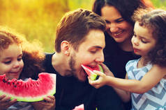 快乐的家庭在绿色花园里野餐。笑笑的人吃西瓜。健康食品概念。双胞胎姐妹