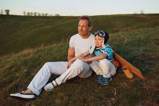 父亲和儿子我坐在草地上在日落的自然.