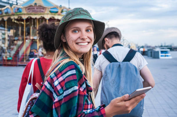 美丽的年轻女子手持智能手机和微笑的相机, 而花时间与朋友在游乐园