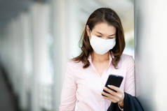在城市里，漂亮的中年工作女商人戴着医疗保护面罩站在人行道上。她手里拿着智能手机。空气污染危机中的医疗理念.