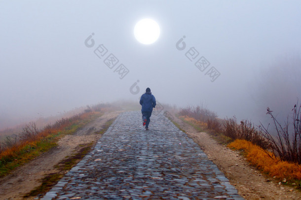 孤独的人在雾的秋天早晨上向着太阳运行