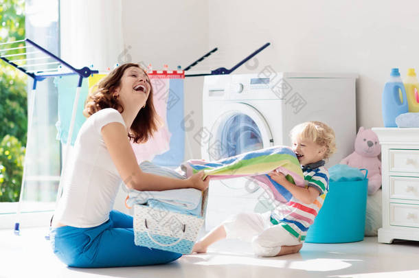 母亲和孩子在洗衣房里用洗衣机或滚筒烘干机。家庭琐事。现代家庭设备和洗涤洗涤剂在<strong>白色阳光</strong>的家。烘干机架清洗洗衣服. 