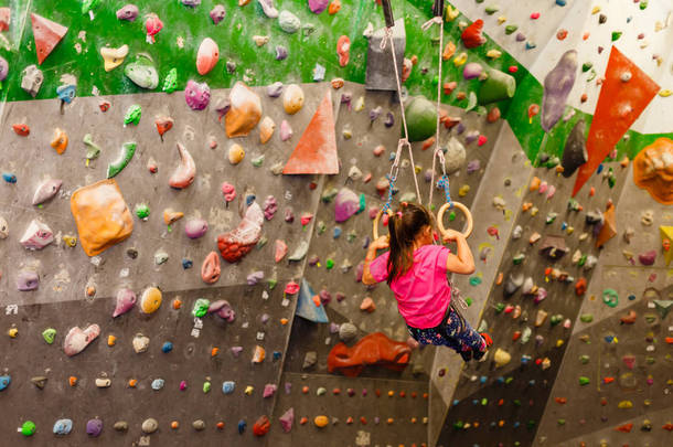 穿着运动服的小<strong>女孩</strong>在体育馆的墙上做运动戒指的练习。健康生活方式的概念从年轻的年龄。儿童运动.