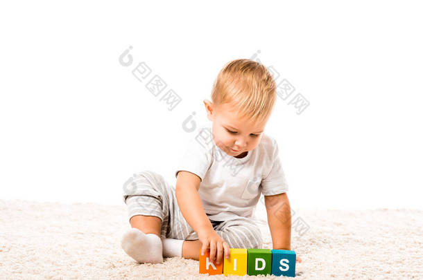 可爱的幼儿男孩玩彩色立方体与文字地毯上孤立的白色