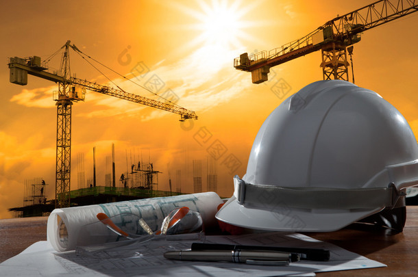 Safety helmet and architect pland on wood table with sunset scen