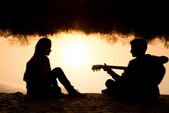 一个年轻的男孩和女孩在沙滩上用一把吉他的剪影