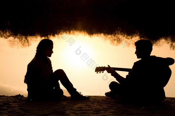 一个年轻的男孩和女孩在沙滩上用一把<strong>吉他</strong>的<strong>剪影</strong>