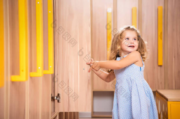 微笑可爱的孩子打开更衣室在幼儿园衣帽间