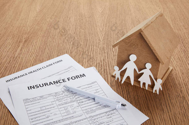 保险形式特写、保险健康理赔表、钢笔、小房子和剪纸家庭在木桌上