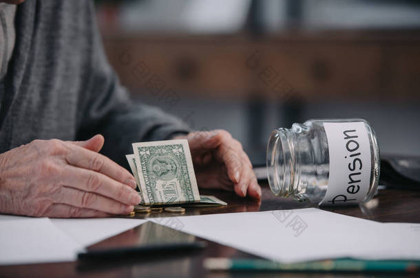 裁剪视图的高级男子坐在桌子上的钱和玻璃瓶与 