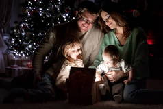 父母与孩子被认为是一个神奇的礼物在圣诞节前夕圣诞树下的壁炉