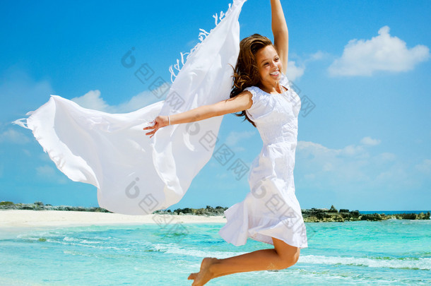 在海滩上跳跃的白色围巾的漂亮女孩