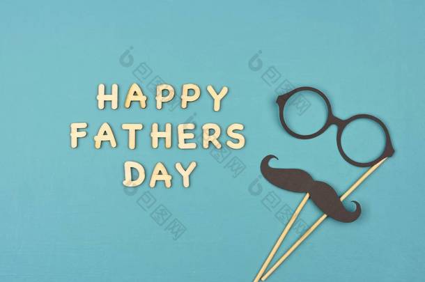 快乐的父亲节用胡子和眼镜的木制字母。蓝色背景上的顶部视图.