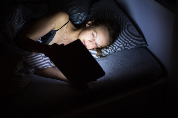年轻女子深夜在她床上使用她的平板电脑