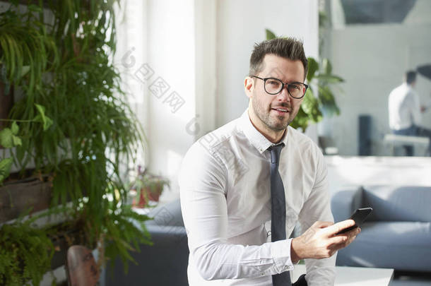 商人坐在办公室里用手机和短信拍摄的肖像. 