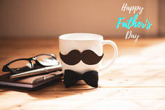 快乐的父亲日概念。咖啡杯带黑色纸胡子和钢笔, 笔记簿, 眼镜在木桌背景上.
