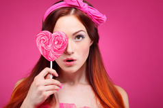 美丽快乐的红头发的女孩与粉红的底色上的大糖果的肖像